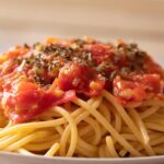 Pasta al pomodoro con sugo rosso ricco, guarnita con basilico fresco su un piatto bianco.